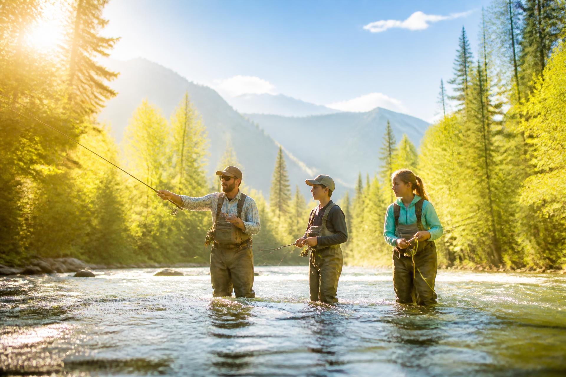 A guide and two teenagers fly fishing in a sunlit mountain river